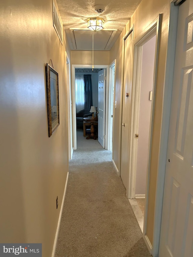 hall with light carpet, attic access, baseboards, and visible vents
