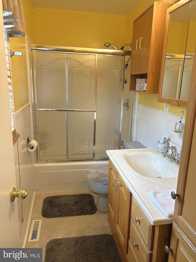 full bathroom featuring tile walls, toilet, visible vents, shower / bath combination with glass door, and vanity