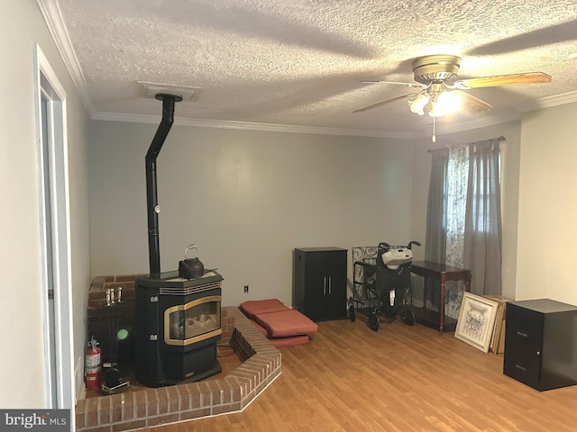interior space featuring a textured ceiling, ceiling fan, crown molding, wood finished floors, and a wood stove