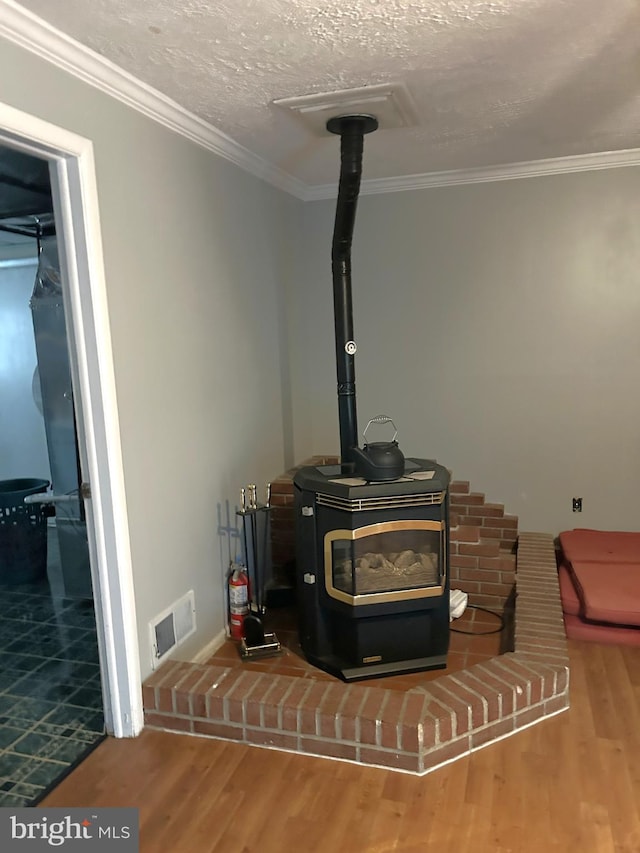 interior details featuring a wood stove, crown molding, visible vents, and wood finished floors