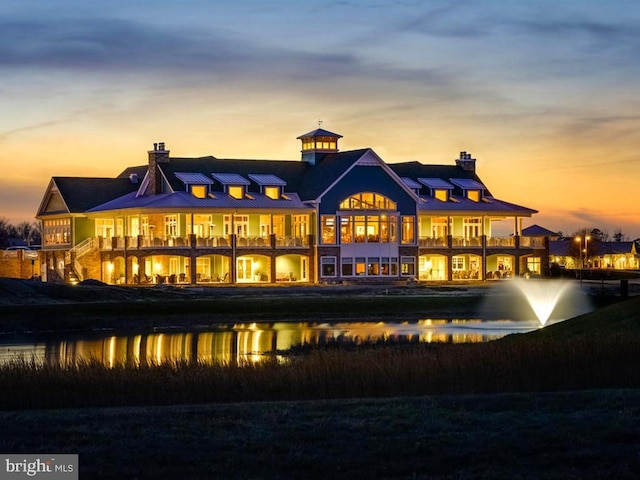 back of property with a standing seam roof, a chimney, a balcony, and a water view