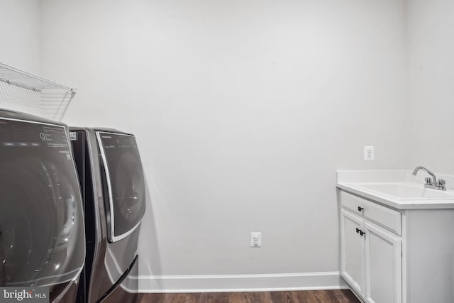 washroom with washing machine and clothes dryer, cabinet space, a sink, baseboards, and dark wood-style floors