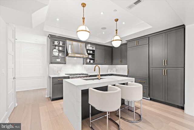kitchen with light countertops, visible vents, wall chimney range hood, a sink, and light wood-type flooring