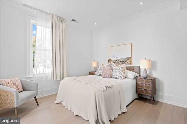bedroom featuring light wood-type flooring, baseboards, visible vents, and ornamental molding