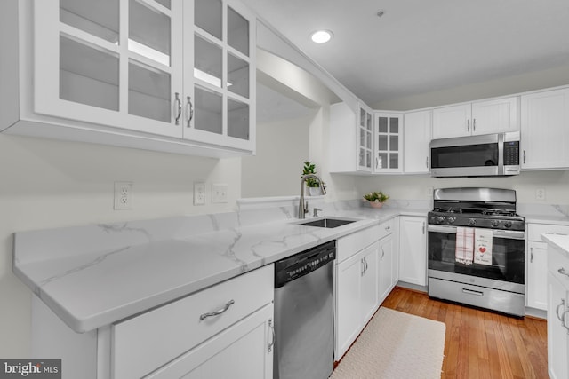 kitchen featuring stainless steel appliances, light stone countertops, white cabinetry, and a sink