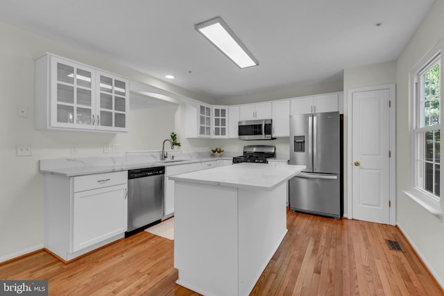 kitchen with appliances with stainless steel finishes, a sink, light wood-type flooring, visible vents, and glass insert cabinets
