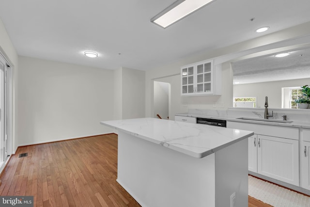 kitchen featuring a sink, a center island, white cabinetry, visible vents, and glass insert cabinets