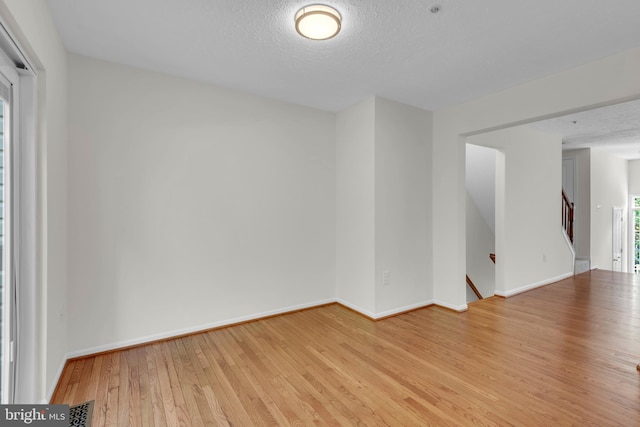 unfurnished room with light wood-type flooring, a textured ceiling, baseboards, and visible vents
