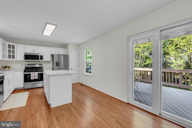 kitchen with a kitchen island, glass insert cabinets, light wood-style floors, light countertops, and stainless steel appliances