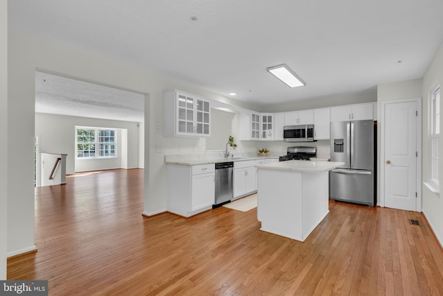 kitchen featuring light countertops, appliances with stainless steel finishes, glass insert cabinets, and light wood-style floors