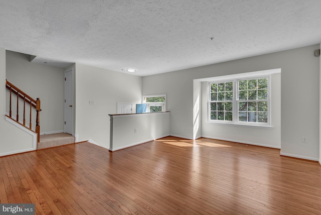 unfurnished living room with hardwood / wood-style floors, stairs, a textured ceiling, and a wealth of natural light