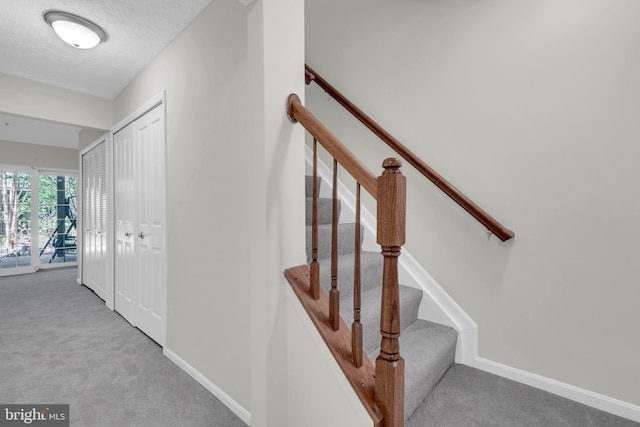 staircase featuring carpet flooring, a textured ceiling, and baseboards