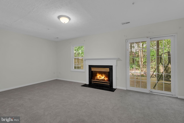unfurnished living room with a fireplace with flush hearth, carpet, a textured ceiling, and visible vents