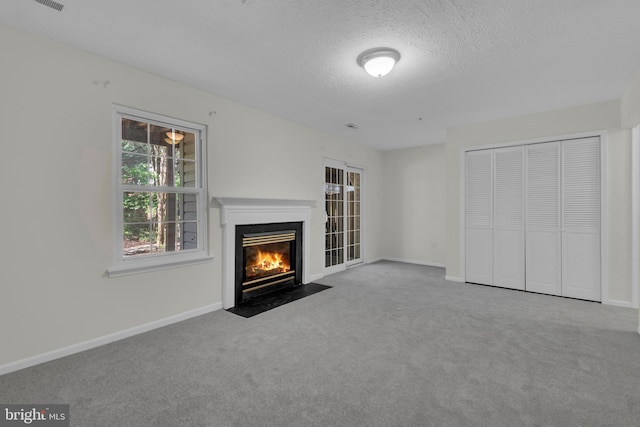 unfurnished living room with baseboards, a fireplace with flush hearth, carpet, and a textured ceiling