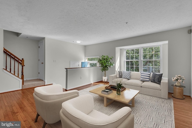 living room with a textured ceiling, baseboards, stairs, and wood finished floors