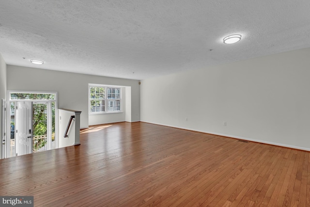 unfurnished living room with baseboards, hardwood / wood-style flooring, and a textured ceiling