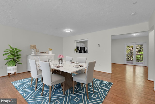 dining space featuring light wood-style floors, a textured ceiling, and baseboards