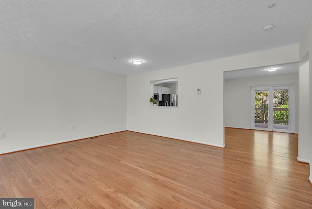 empty room featuring baseboards, a textured ceiling, and light wood-style flooring