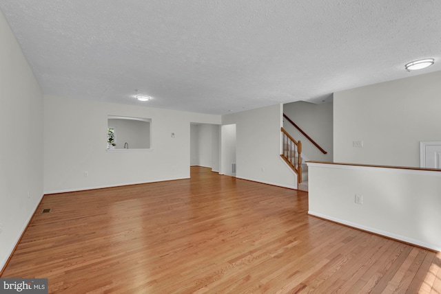 unfurnished room with baseboards, a textured ceiling, light wood finished floors, and stairs