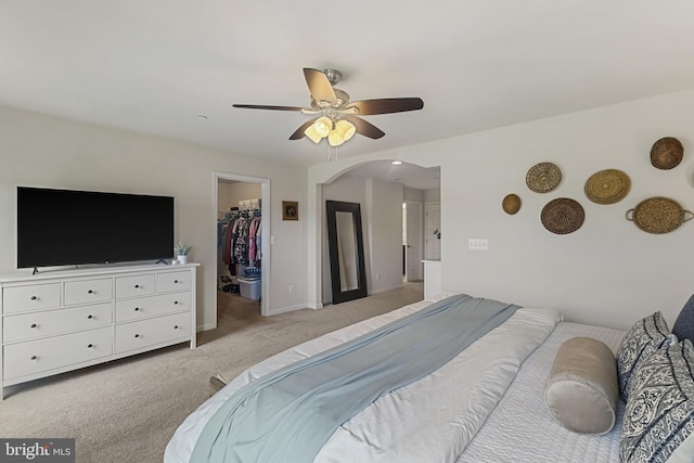 bedroom featuring a ceiling fan, a walk in closet, light carpet, baseboards, and arched walkways