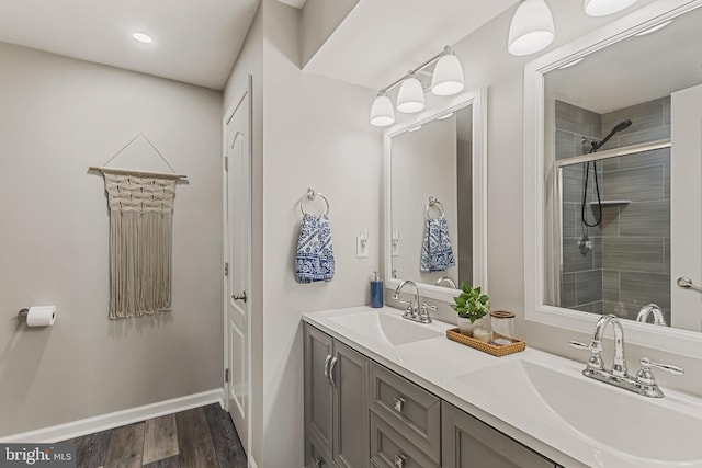 bathroom featuring a tile shower, double vanity, a sink, and wood finished floors
