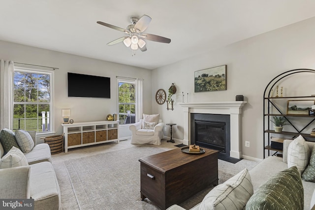 carpeted living area with baseboards, ceiling fan, and a fireplace with flush hearth