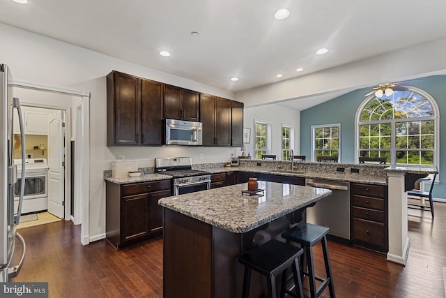 kitchen featuring a breakfast bar area, appliances with stainless steel finishes, a sink, dark wood-style floors, and a peninsula