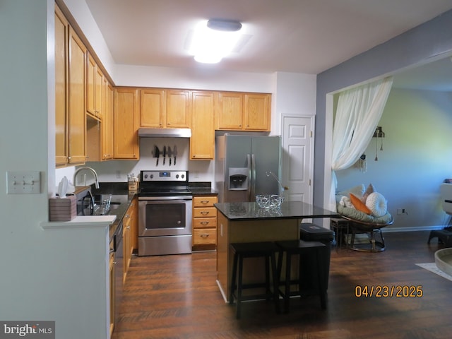 kitchen with stainless steel appliances, a breakfast bar, dark countertops, a sink, and dark wood-style flooring