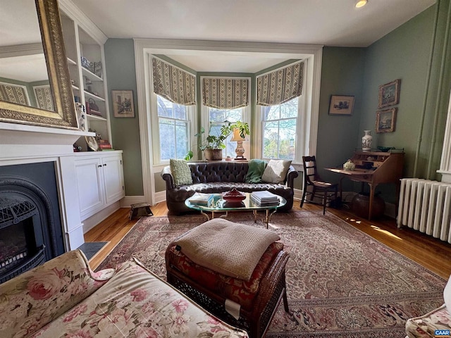 living area with radiator, light wood-type flooring, a fireplace, and baseboards