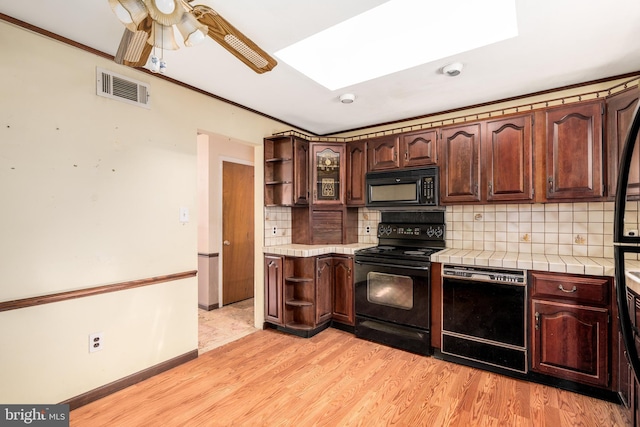 kitchen with open shelves, light wood-style flooring, tile counters, visible vents, and black appliances