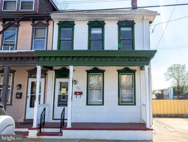 italianate home featuring a chimney, covered porch, and fence