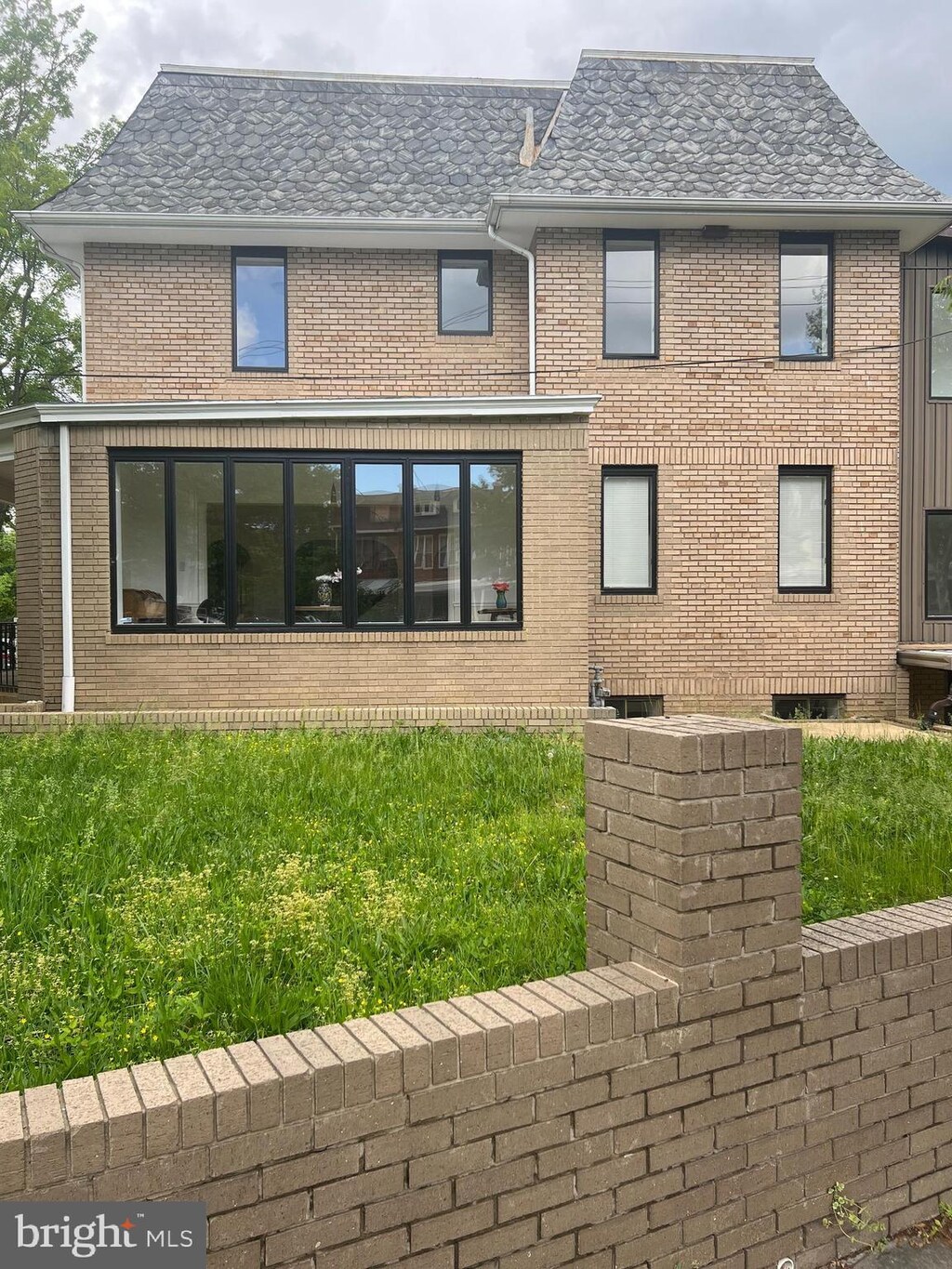 back of house featuring brick siding and roof with shingles