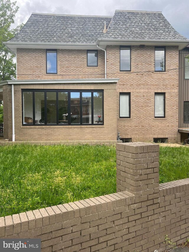 back of house featuring brick siding and roof with shingles