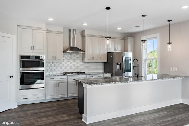 kitchen with wall chimney range hood, stone counters, stainless steel appliances, and a sink