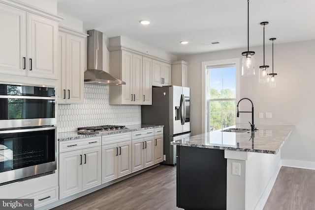 kitchen with appliances with stainless steel finishes, tasteful backsplash, wood finished floors, a sink, and wall chimney exhaust hood