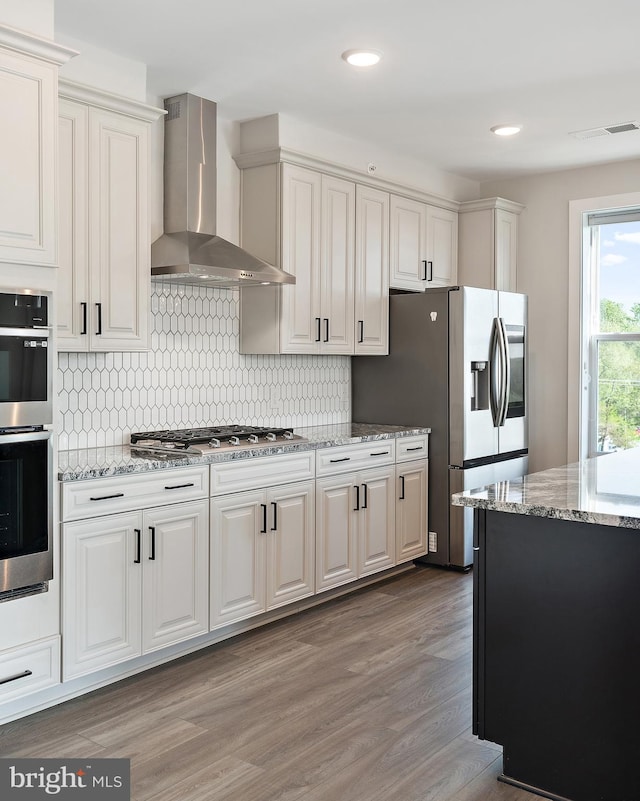 kitchen featuring visible vents, wood finished floors, wall chimney exhaust hood, tasteful backsplash, and appliances with stainless steel finishes