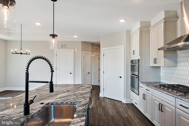 kitchen featuring wall chimney range hood, dark wood-style flooring, a sink, stainless steel appliances, and visible vents