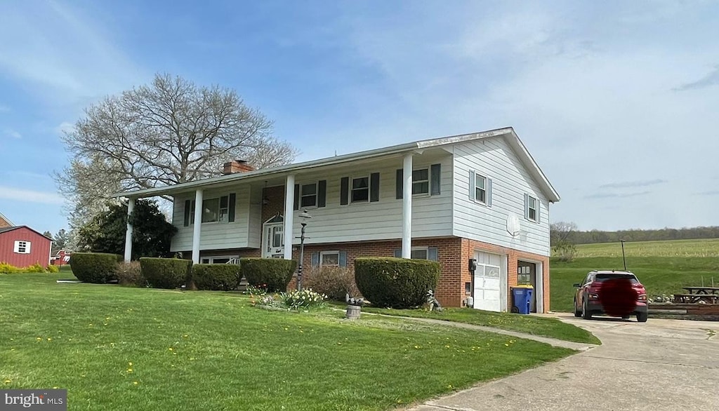 split foyer home featuring an attached garage, a front lawn, brick siding, a chimney, and driveway