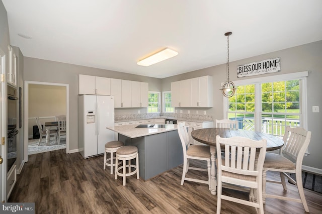 kitchen with white cabinets, dark wood-style floors, a breakfast bar, a kitchen island, and white fridge with ice dispenser