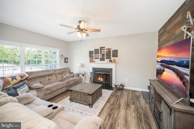 living room with a fireplace with flush hearth, ceiling fan, baseboards, and wood finished floors