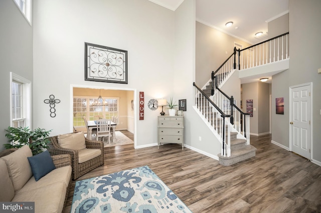 living area featuring crown molding, stairs, wood finished floors, baseboards, and a high ceiling