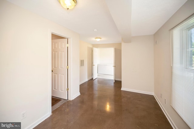 hall featuring concrete flooring, visible vents, and baseboards