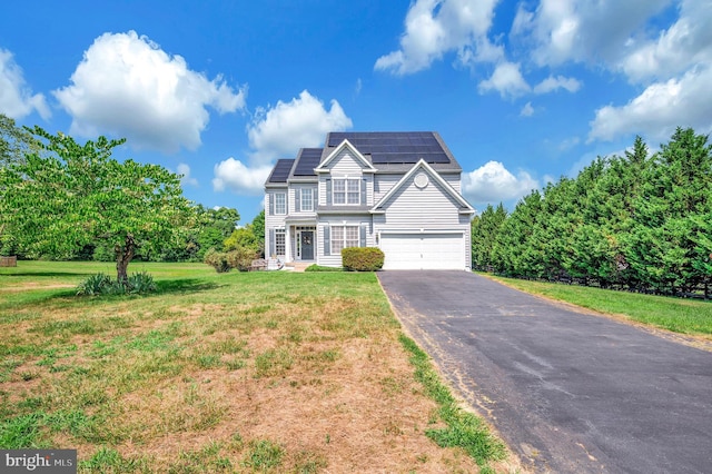 traditional home with roof mounted solar panels, driveway, an attached garage, and a front yard