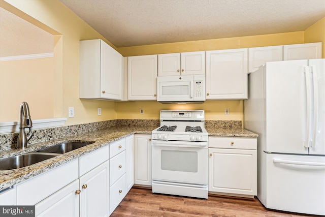 kitchen with white appliances, light wood-type flooring, white cabinets, and a sink