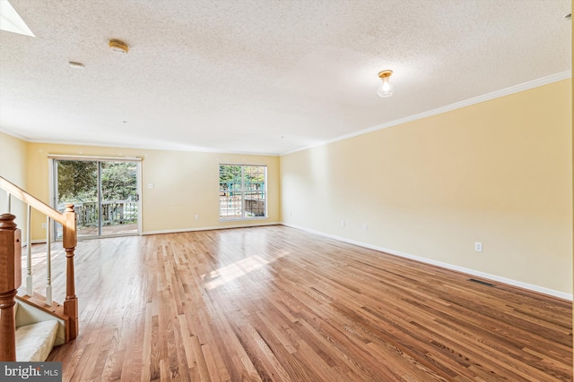 unfurnished living room with a textured ceiling, crown molding, light wood-style flooring, stairway, and baseboards