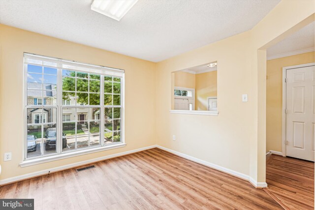 empty room with baseboards, visible vents, wood finished floors, and crown molding
