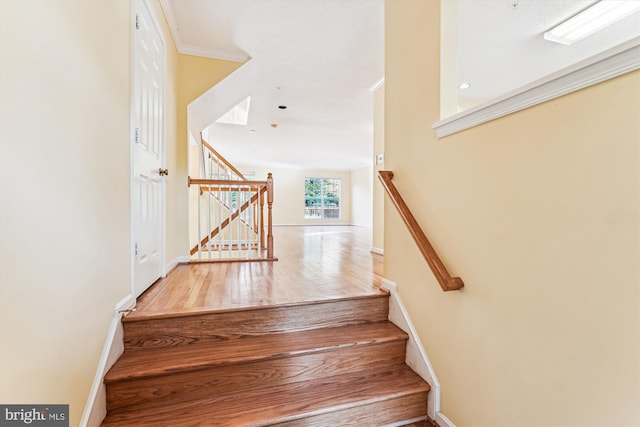 staircase featuring baseboards, wood finished floors, and crown molding