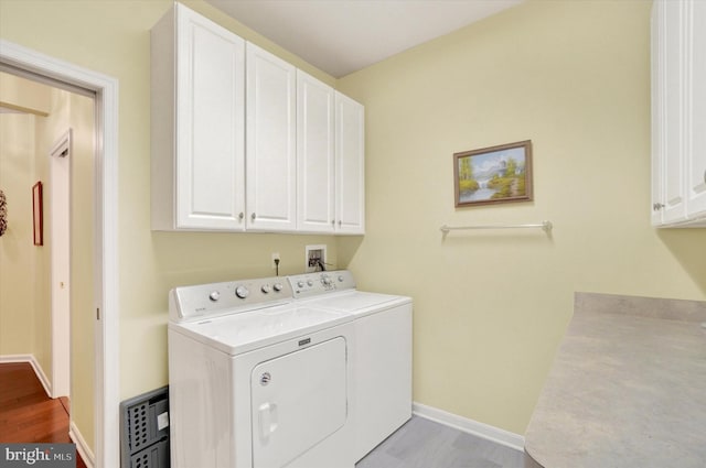 clothes washing area featuring cabinet space, separate washer and dryer, baseboards, and wood finished floors