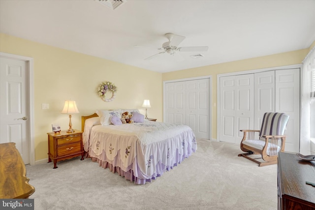 bedroom with visible vents, two closets, ceiling fan, and light colored carpet