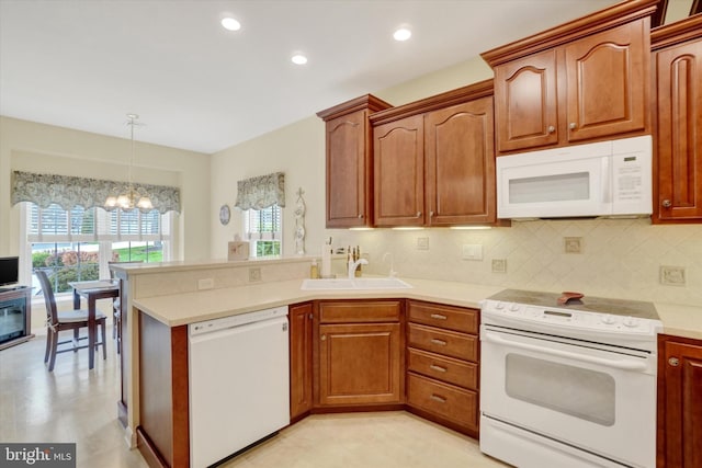 kitchen with a peninsula, white appliances, light countertops, a sink, and a notable chandelier